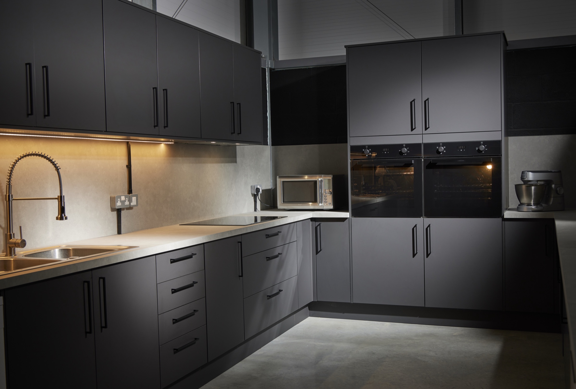 The Hopclover One production kitchen: graphite units, stone worktops and under-cabinet lighting